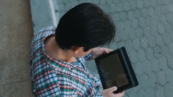 Hombre en una camisa a cuadros utiliza la tableta al aire libre — Vídeos de Stock