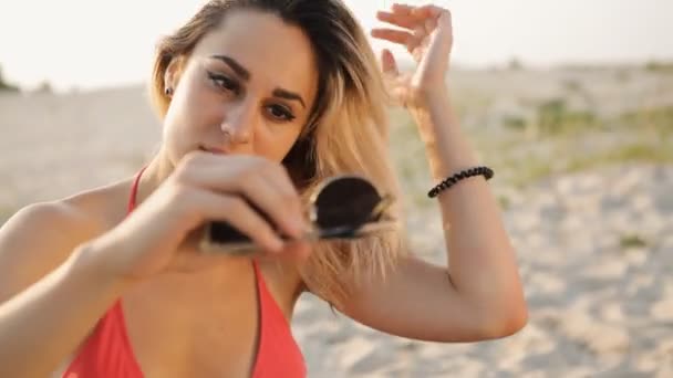 Sexy meisje op het strand rechtzetten haar zonnebril gebruiken als een spiegel — Stockvideo