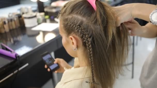 Chica utiliza el teléfono inteligente en peluqueros, mientras que el trabajo de peluquería en el pelo clientes — Vídeo de stock