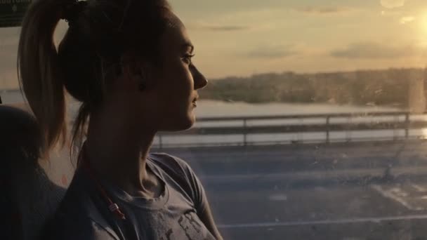 Женщина путешествует в автобусе, глядя в окно на закате — стоковое видео