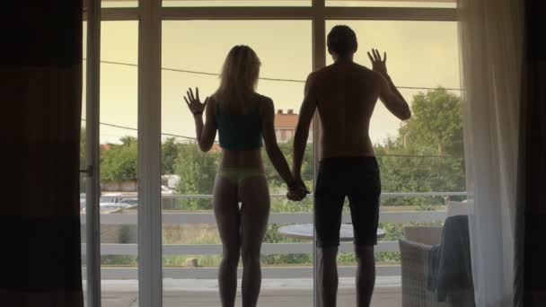 Мужчина и женщина силуэта держатся за руки и смотрят в окно — стоковое видео