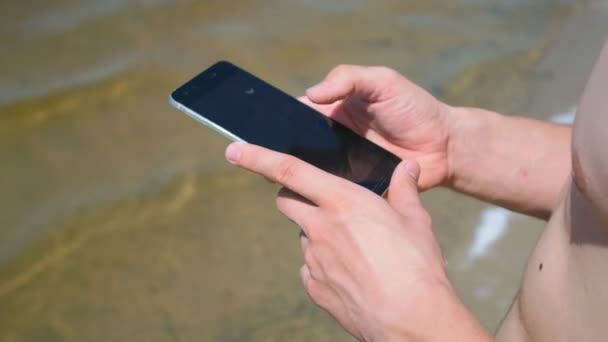 Primer plano del hombre usando su teléfono inteligente en la playa — Vídeo de stock
