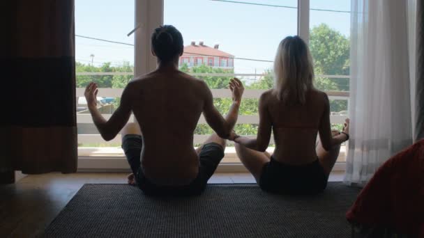 Pareja haciendo yoga contra la ventana — Vídeo de stock