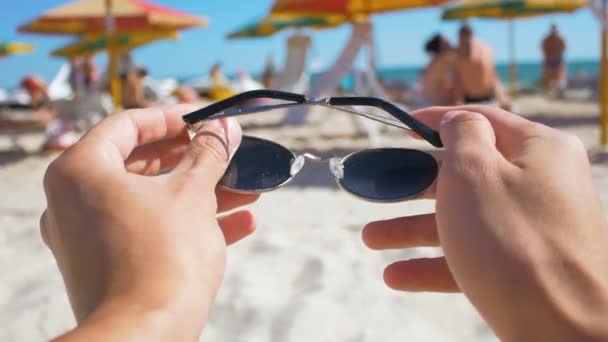 Чоловік одягає сонцезахисні окуляри на пляжі вид від першої особи — стокове відео