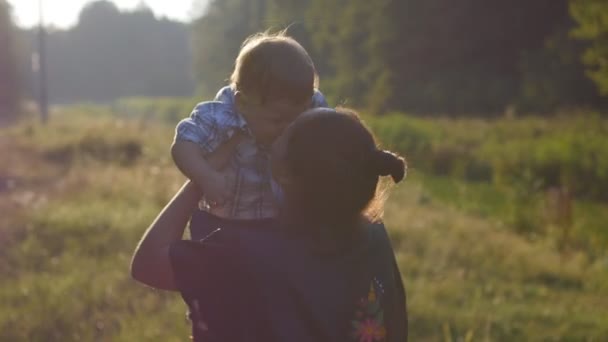 Happy mother holding her baby in her hands and spinning at sunset in the garden — Stock Video