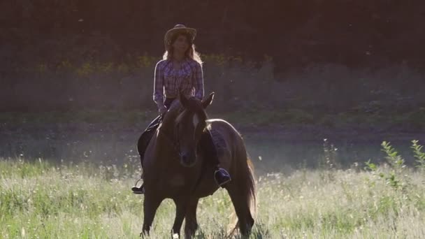 Mädchen mit Hut reitet bei Sonnenuntergang in Zeitlupe auf einem Pferd — Stockvideo