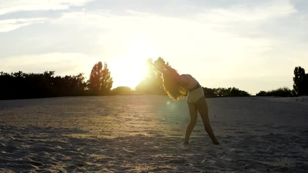 Sexy meisje doen achteruit walkover op het zand bij zonsondergang — Stockvideo