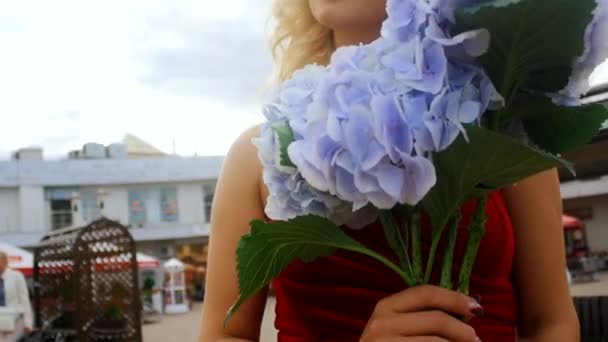 Close-up de mulher loira em um vestido vermelho com um buquê de flores em suas mãos — Vídeo de Stock