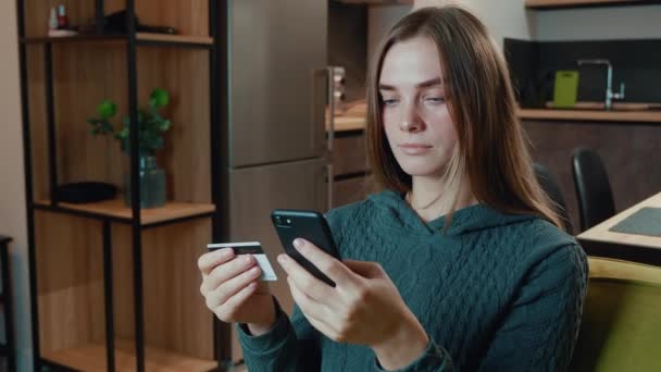 Junge Frau shoppt online auf dem Sofa zu Hause. Lächelnde Frau beim Online-Banking mit Smartphone und Kreditkarte zu Hause. Einfaches Bezahlen mit digitalem Gerät. — Stockvideo