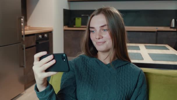 Χαμογελώντας χαλαρή νεαρή γυναίκα κατέχουν smartphone βλέποντας ιστορίες social media βίντεο siting στον καναπέ στο σαλόνι στο σπίτι. — Αρχείο Βίντεο