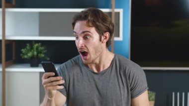 Heyecanlı genç adam akıllı telefonundaki mesajla seviniyor. Cep telefonuna bakan mutlu erkek zaferi kutluyor. Şanslı kumarbazın portresi evet işareti yapıyor..