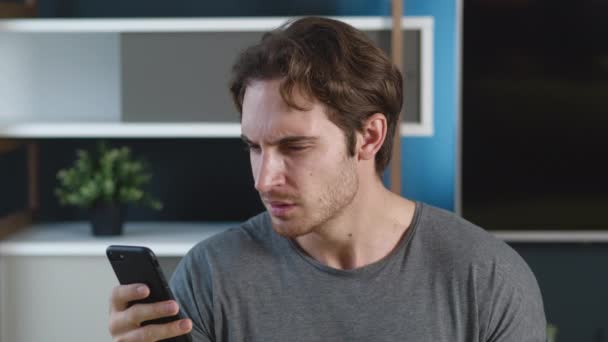 Ο άνθρωπος είναι σοκαρισμένος τρομερό μήνυμα στο smartphone του στο σπίτι διαμέρισμα φόντο. Δυσάρεστα έκπληκτος νεαρός άνδρας αντιδρώντας μήνυμα στο κινητό του τηλέφωνο. — Αρχείο Βίντεο