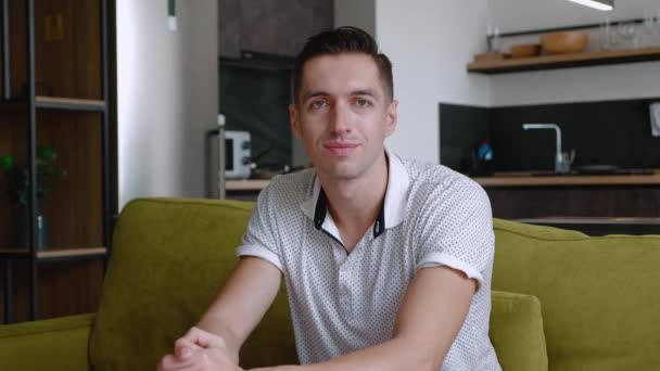 Portrait de l'homme heureux se repose tout en étant assis sur le canapé à la maison. Un jeune homme aime le style de vie en regardant la caméra assis sur un canapé confortable dans son appartement. — Video