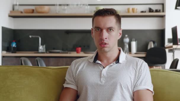 Porträt eines aggressiven Mannes, der schreit, während er zu Hause auf dem Sofa sitzt. Ein wütender junger Mann zeigt Aggression. Emotionaler Stress. Aufschlüsselung. — Stockvideo