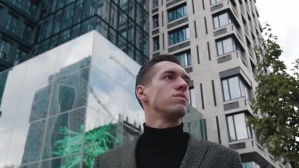 Retrato de homem de negócios pensativo vestindo terno coloca óculos de sol olhando para fora, enquanto está perto de edifício de escritório moderno. Jovem empresário masculino olhando ao redor no centro da cidade. Parece bem sucedido. — Vídeo de Stock