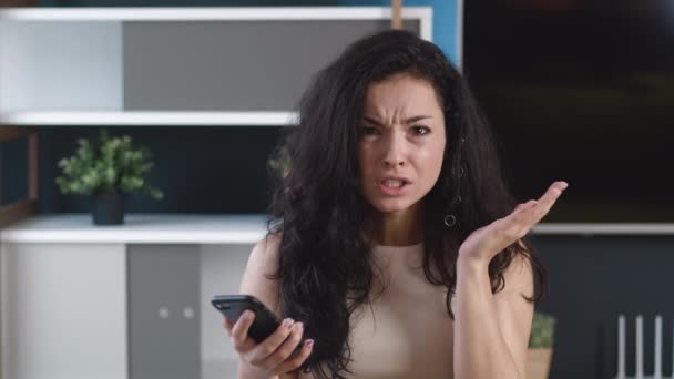 Znepokojená žena čte špatné zprávy ve svém smartphonu. Šokovaná mladá žena drží mobilní telefon v rukou doma nebo v kanceláři. — Stock video