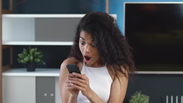 Happy african american woman looking in smartphone feel surprised, saying WOW and makes Yes gesture. Celebrating success victory. Excited black female winner hold mobile phone amazed with good news. — Stock Video