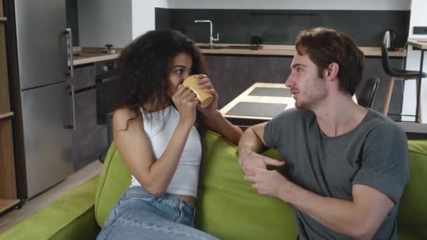 Heureux jeune couple multiracial homme et femme assis sur un canapé confortable et parlant dans le salon. — Video