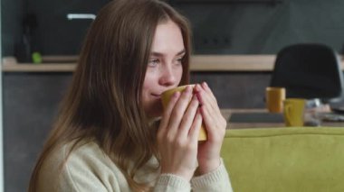 Yakın plan genç bayan evdeki rahat kanepede otururken lezzetli sıcak çayın tadını çıkarıyor. Güzel düşünceli kadın portresi oturma odasında bir fincan lezzetli kahveyle kanepede dinleniyor..