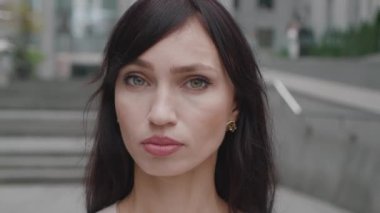 Kentin arka planında kameraya bakan kendinden emin genç bir iş kadını. Şehir caddesinde duran güzel genç bayan portresi. Gerçek insanlar..