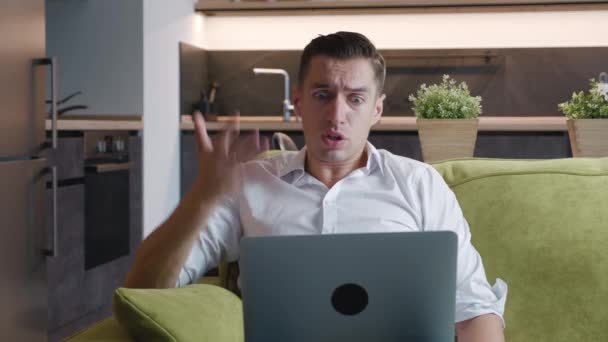 Wściekły człowiek mający wideo rozmowy online za pośrednictwem laptopa komputera z przyjacielem pokazuje urazę i agresywne emocje do przeciwnika leżąc na kanapie w domu. — Wideo stockowe