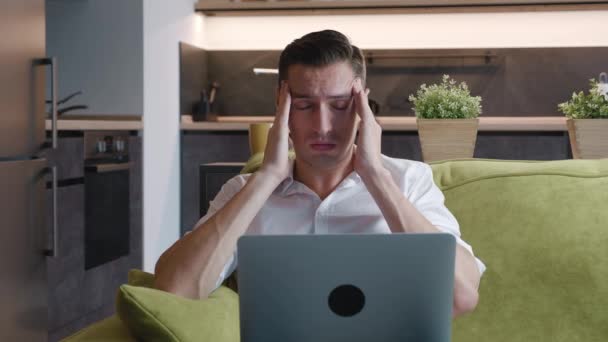 ソファに横たわっ自宅でノートパソコンで作業中にストレスを探してハンサムな若い男。自宅からノートパソコンでリモートで作業しながら、過労のビジネスマンの肖像画。男性は頭痛がします. — ストック動画
