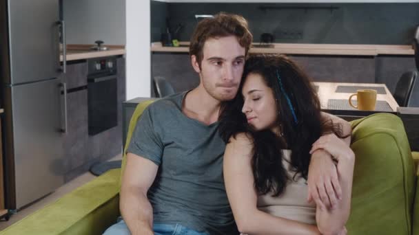 Feliz pareja joven son tiernamente abrazar y sentarse en el sofá en casa. El marido abraza a su esposa sensualmente. — Vídeos de Stock