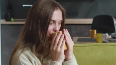 Kazaklı genç bir kadın evdeki rahat kanepede otururken lezzetli sıcak çayın tadını çıkarıyor. Güzel düşünceli kadın portresi oturma odasında bir fincan lezzetli kahveyle kanepede dinleniyor..