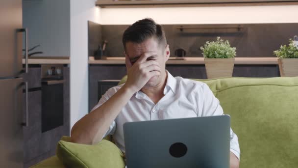 Smutny człowiek freelancer wygląda na zestresowanego podczas pracy nad laptopem martwiąc się o problemy leżąc na kanapie w domu. Portret przepracowanego płaczącego biznesmena pracującego zdalnie w laptopie z domu. — Wideo stockowe