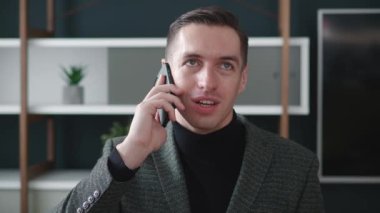 Modern ofiste cep telefonuyla konuşan kendinden emin iş adamının portresi. Neşeli erkek girişimcinin iş yerinden telefon görüşmesi yapması yakındır..