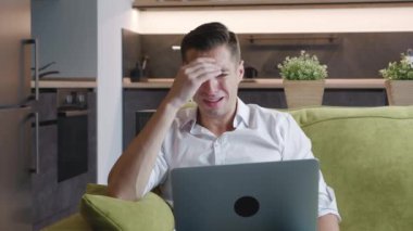 Üzgün adam dizüstü bilgisayarı üzerinde çalışırken stresli görünüyor. Evdeki kanepede yatarken problemler için endişeleniyor. Evden bilgisayarla uzaktan çalışan çok çalışan ağlayan iş adamının portresi..