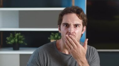 Şok olmuş genç adam gördüklerinden tiksiniyor. Nahoş bir şekilde şaşırmış erkek eliyle ağzını kapatır. Arka planda ev ya da ofis dairesi