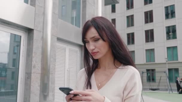 Jovem mulher de negócios bonita usando smartphone e andando nas ruas da cidade do centro da cidade. Negócios feminino comutação navegação redes sociais feliz estilo de vida ao ar livre. — Vídeo de Stock