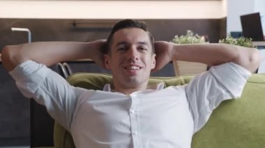 Evdeki rahat kanepede dinlenen sakin genç adam. Mutlu iş adamı temiz hava soluyor kanepede elleri başının arkasında dinleniyor stressiz huzurlu bir günün tadını çıkar..