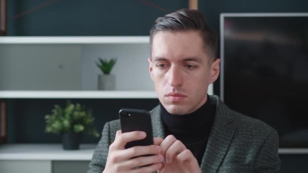 ストレスを受けたビジネスマンは、現代のオフィスの背景にスマートフォンを使用している間にショックを受けます。携帯電話で悪いニュースを読むことを心配し、不快な驚きと怖いビジネス男性. — ストック動画