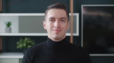 Kameraya bakan sevimli profesyonel iş adamı. Modern ofiste poz veren mutlu genç erkek tasarımcının portresi..