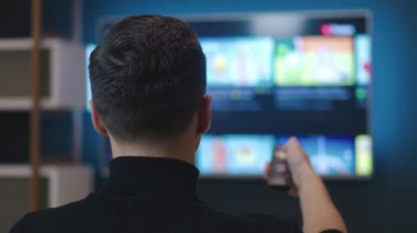 Evdeki kanepede oturup televizyon izleyen tanınmamış bir adam. Akşamları evdeki kanepede otururken uzaktan kumandalı bir televizyon kanalı ya da film seçen genç adamın arka görüntüsü.