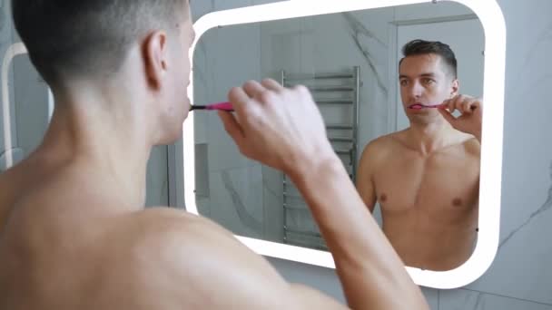 Miroir reflet de jeune homme nu se brossant les dents avec une brosse à dents et du dentifrice le matin en faisant la routine d'hygiène. — Video