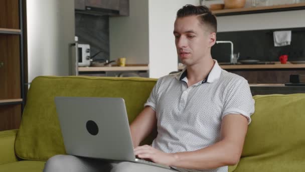 Fiatal férfi szabadúszó használ laptop eszköz kanapén otthon iroda, portré a férfi dolgozik távolról számítógép a lakásban — Stock videók