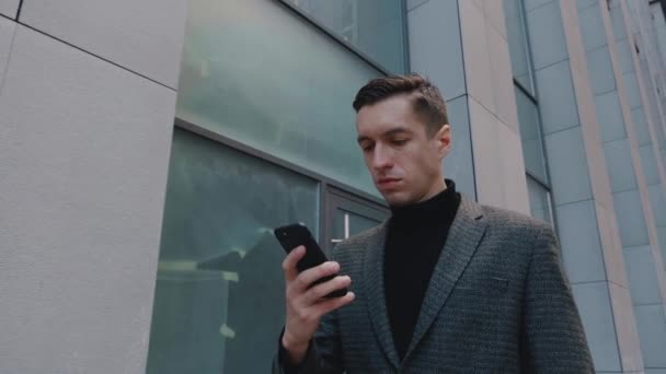 Empresario de confianza usando el teléfono móvil. Hombre joven en traje mensajes de texto, engañando a su Smartphone mientras camina en el Distrito de Oficina. Negocios. Redes sociales. Gente. Aplicaciones. — Vídeo de stock