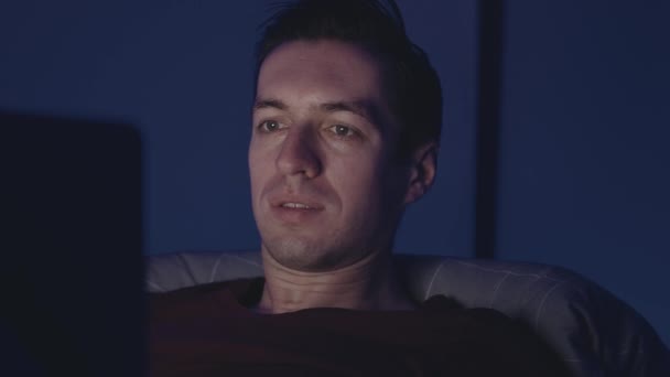Genç adam geceleri laptopta film seyrediyor. Erkek, geceleri yatak odasında yatarken dizüstü bilgisayar kullanıyor.. — Stok video