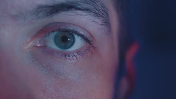 Extrémní detailní záběr mladého muže, který se v noci dívá na film. Detailní odraz v oku světla z obrazovky. — Stock video