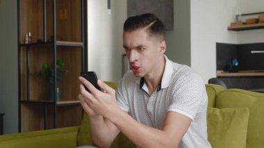 Akıllı Telefon Kullanan Saldırgan Adam. Adam evdeki koltukta otururken cep telefonunda okuduğu mesaja kızgın..