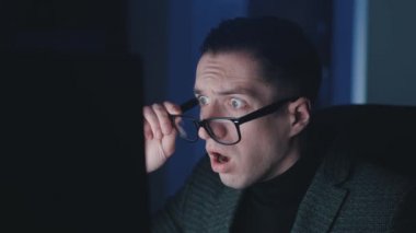 İşadamı gece geç saatlerde bilgisayar dizüstü bilgisayarında çalışırken şok oldu ve şaşırdı. Şaşkınlık içindeki girişimci gözlük takar ve ekrandaki görüntülere şaşırır..