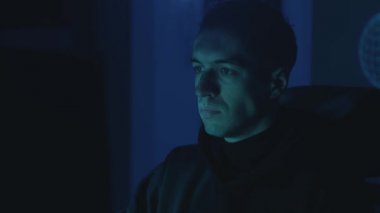 Geceleri ofisteki sunucuya bilgisayar komplosu kuran tehlikeli bilgisayar korsanı portresi. Genç erkek casus karanlık odada bazı yazılımları hackliyor.
