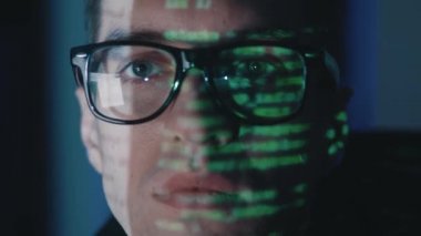 Yakın plan yüz portresi bilişim yazılımı geliştiricisi gözlüklü bilgisayar, geceleri sunucuya siber saldırı. Yeşil program kodu yüze yansıdı. Erkek sanal casus hackleme yazılımı karanlık odada