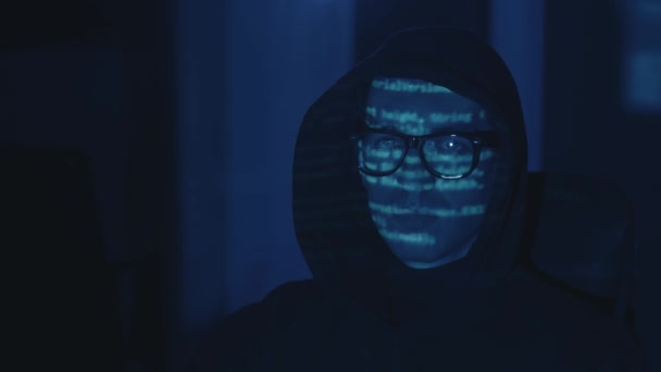 Portret van hooded IT hacker programmeur ontwikkelaar in bril werkende computer, cyber aanval op de server 's nachts. Programmacode weerspiegeld op gezicht. Gevaarlijke mannelijke virtuele spion hacken software in donkere kamer — Stockvideo