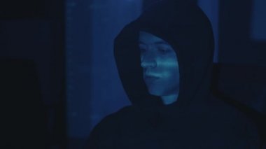 Geceleri ofisteki sunucuya bilgisayar entrikaları düzenleyen kapüşonlu tehlikeli hacker programcısı. Genç erkek casus karanlık odada bazı yazılımları hackliyor.