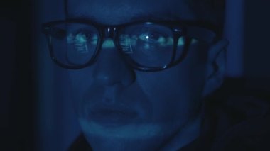 Bilgisayarda çalışan gözlüklü bilgisayar programcısı ve geceleri sunucuya yapılan siber saldırıyla ilgili yüz portresini kapat. Program kodu yüze yansıdı. Erkek sanal casus hackleme yazılımı karanlık odada