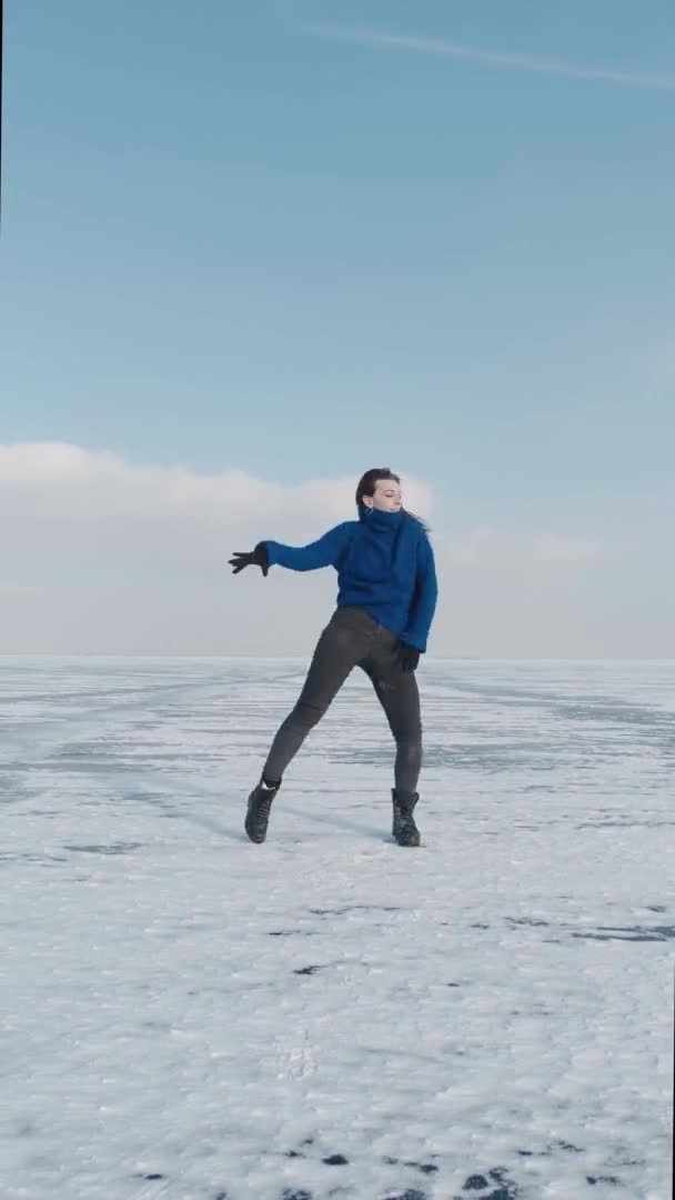 Vídeo vertical de una bailarina profesional milenaria, bailando jazz funk enérgico o hip hop en un lago helado en invierno frío. Mujer hipster baila desafío para las redes sociales en río cubierto de nieve — Vídeo de stock